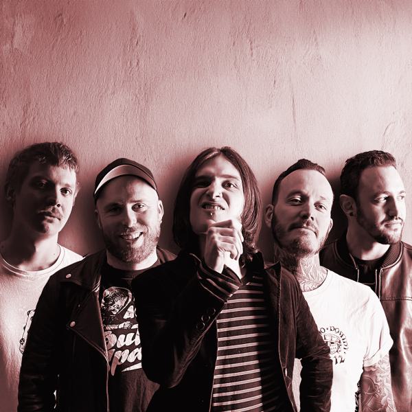 Bansfoto Bakemono Stereo: Fünf Personen stehen eng nebeneinander vor einer hellen Wand. Das Foto ist in warmen Rot- und Sepiatönen gehalten. Die Personen tragen überwiegend dunkle Kleidung, einige haben kurze Haare, eine Person hat schulterlanges Haar. Di